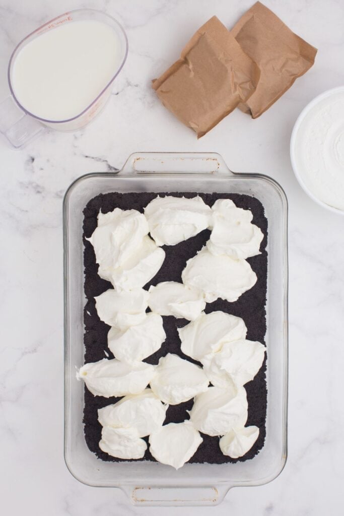 Cream cheese mixture is dolloped on top of the Oreo cookie crust in the glass baking pan.