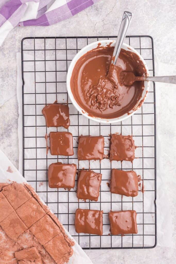 Chocolate pudding and Cool Whip Mix cut into squares and dipped in melted chocolate. Candy squares are placed on a wire rack over a sheet of parchment.