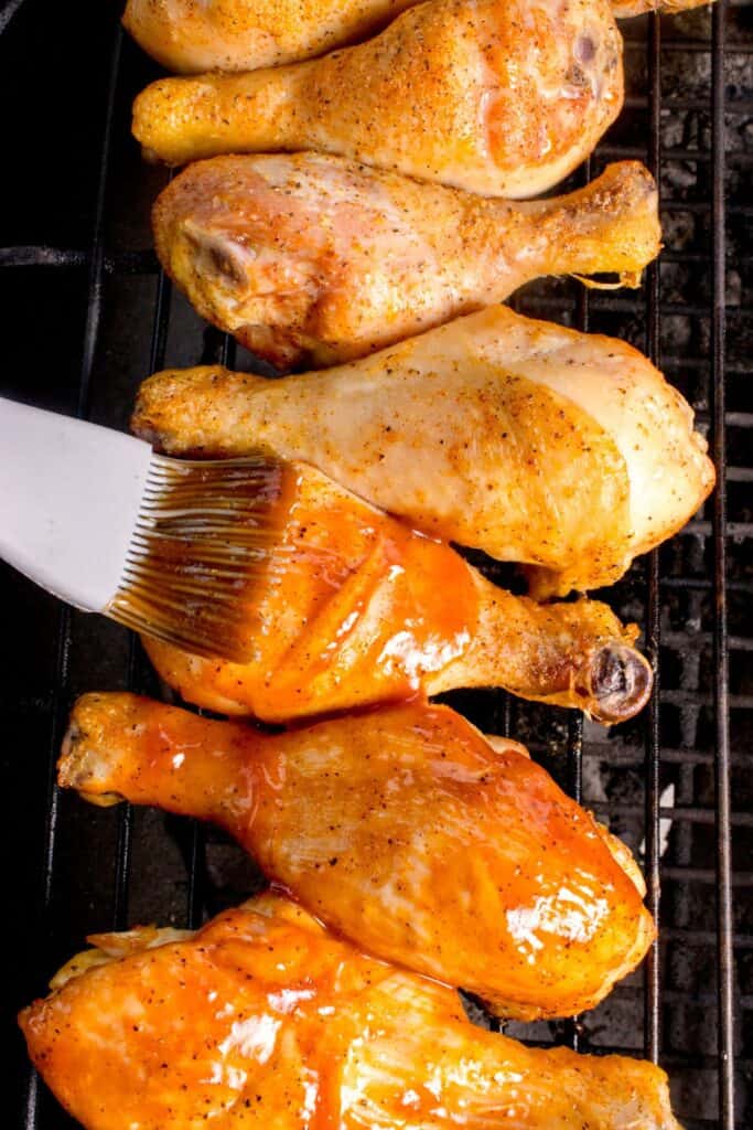 Chicken legs on the grill being brushed with BBQ sauce.