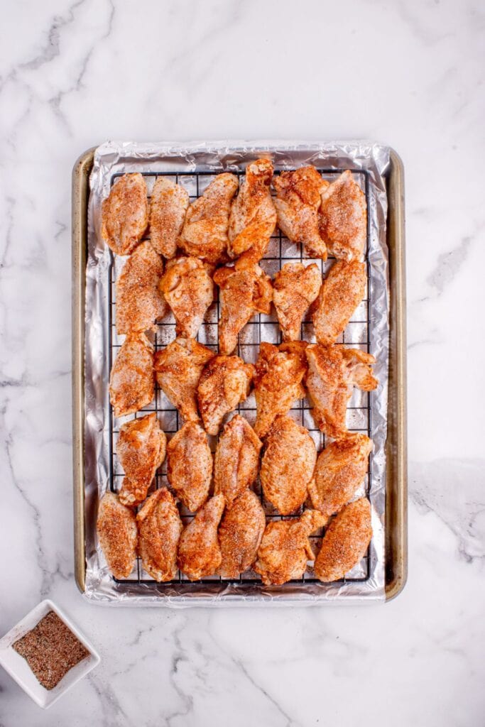 Seasoned chicken wings arranged on a aluminum foil lined baking sheet.