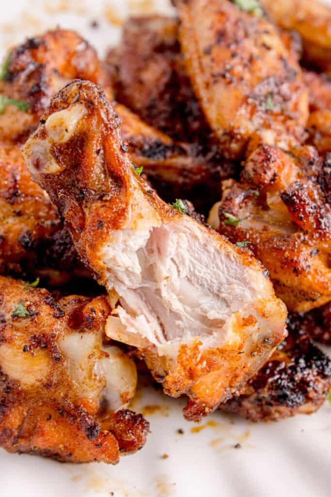 Completed chicken wings on a white dinner plate. A bite is taken out of the wing on top of the pile.
