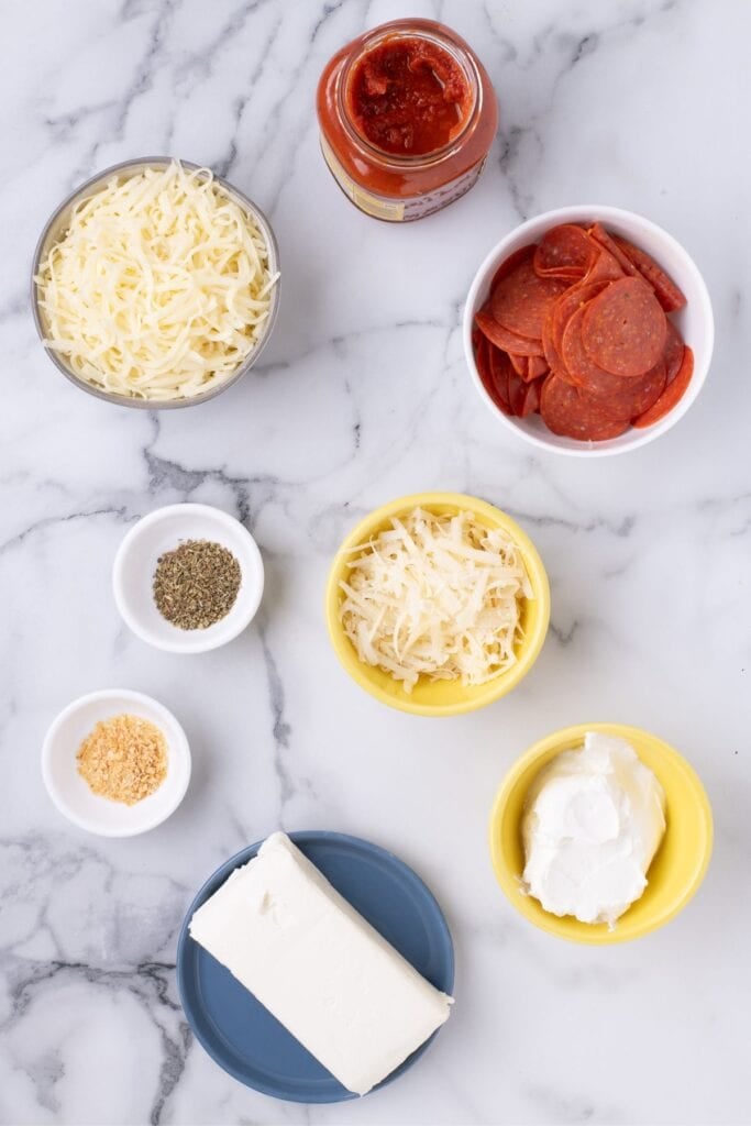 Ingredients for pizza dip: cream cheese, sour cream, dried oregano, dried minced onion, mozzarella cheese, parmesan cheese, pizza sauce, and pepperoni.