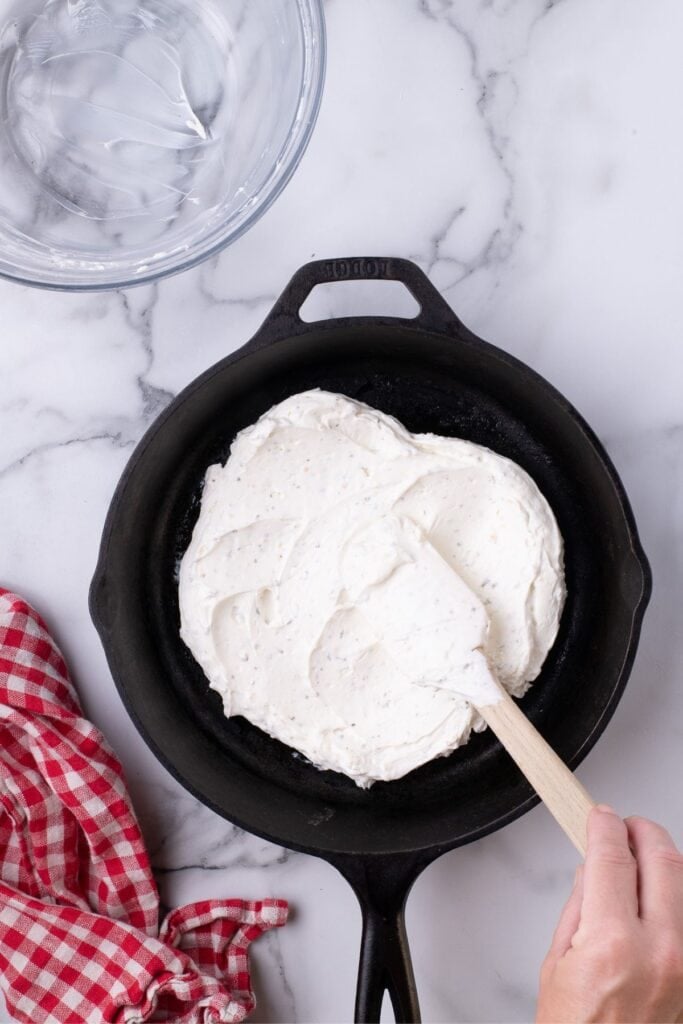 Cream cheese mixture is spread on the bottom of the cast iron pan.