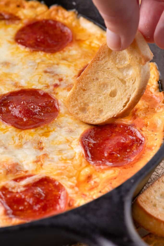 A crostini being dipped in the warm pizza dip.