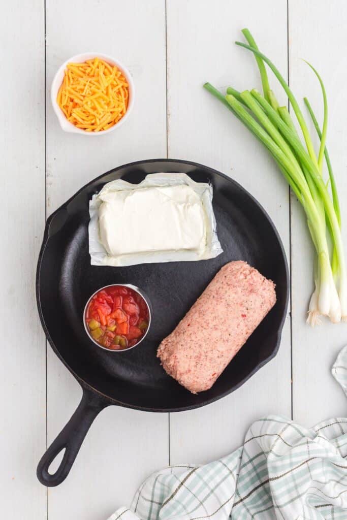 Ingredients for sausage cream cheese dip: breakfast sausage, cream cheese, Rotel, cheddar cheese, and green onions.