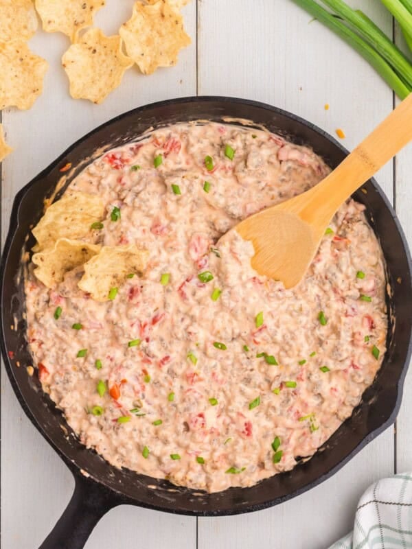 Completed sausage cream cheese dip in cast iron pan with a wooden spatula.
