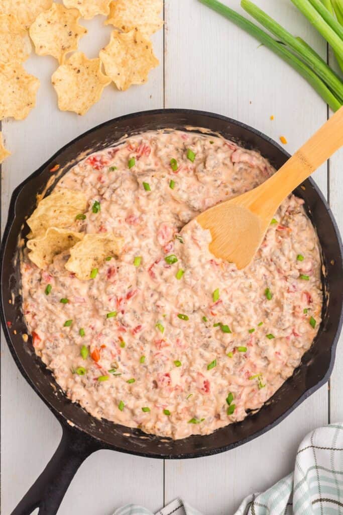 Completed sausage cream cheese dip in cast iron pan with a wooden spatula.