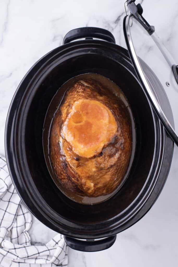 Crock pot insert with a spiral ham placed in it. A glaze has been poured evenly over the top.