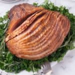 Completed spiral ham on a white serving platter, garnished with a mix of greens.