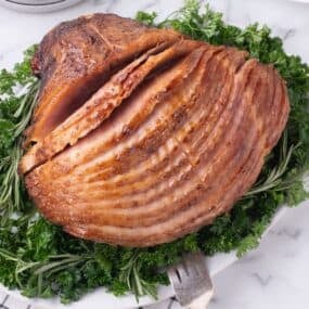 Completed spiral ham on a white serving platter, garnished with a mix of greens.