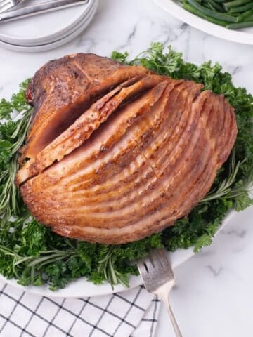 Completed spiral ham on a white serving platter, garnished with a mix of greens.