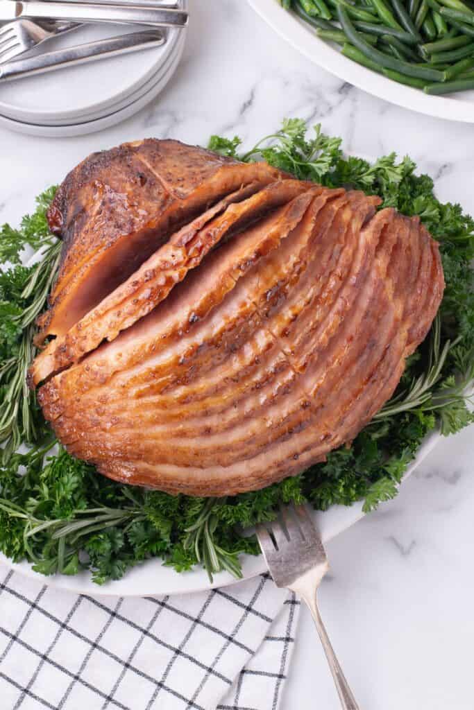 Completed spiral ham on a white serving platter, garnished with a mix of greens.