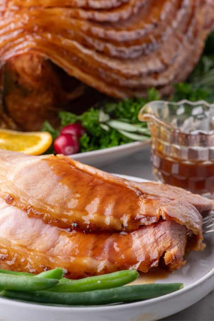 Slices of spiral ham on a white dinner plate in front of the full, cooked spiral ham.