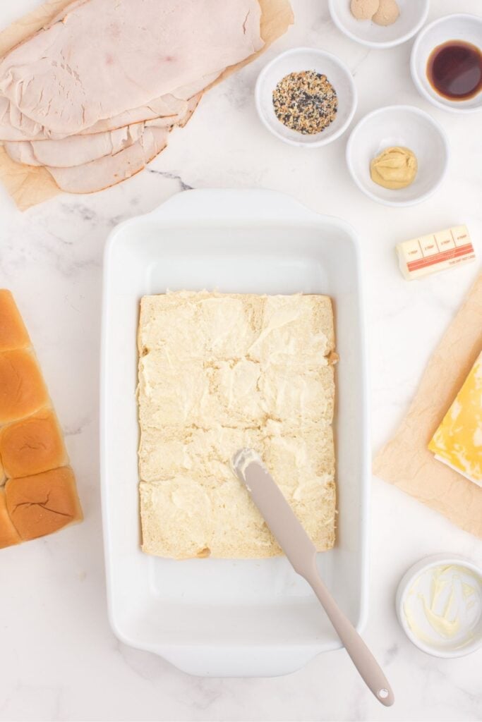 The bread roll loaf is sliced in half and mayo is spread over the base of the rolls.