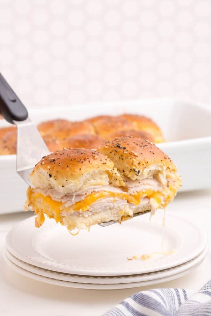 A serving spatula holding two turkey sliders above a white dinner plate.