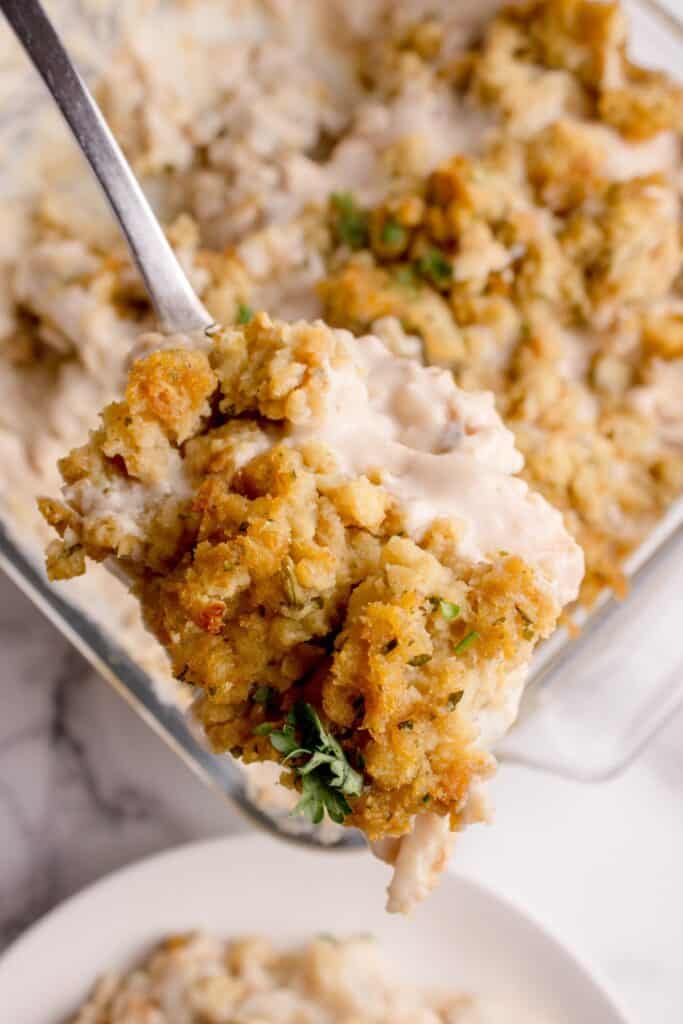 A serving spoon is lifting up a portion of casserole above the baking dish.