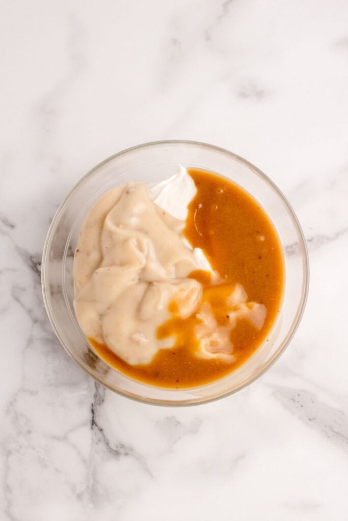Cream of mushroom soup, gravy, and sour cream combined in a glass mixing bowl.