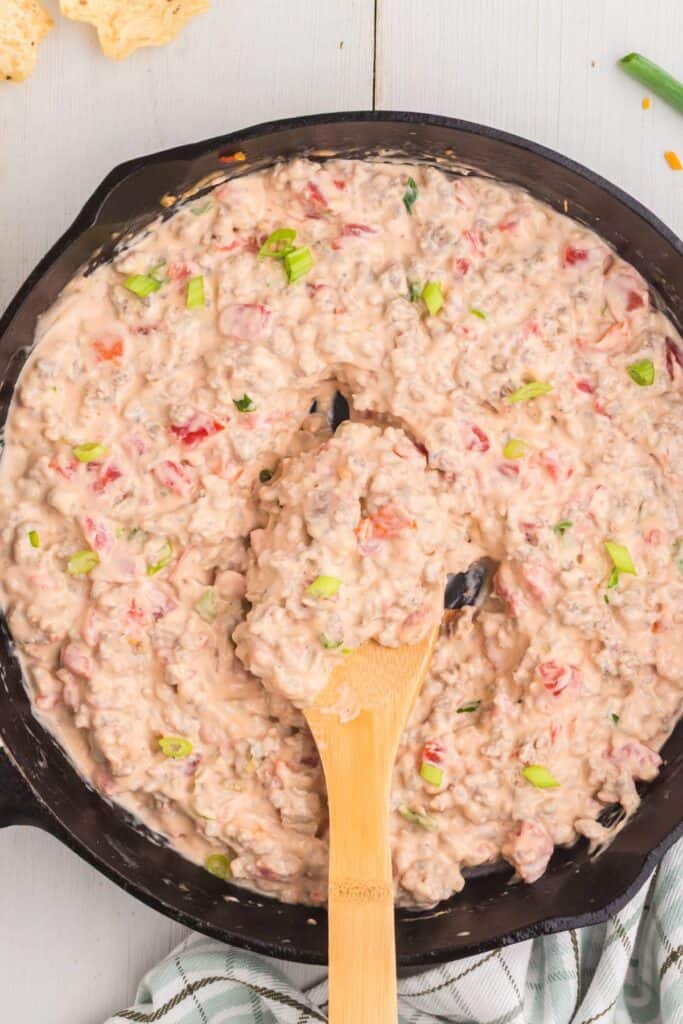 Close up of sausage cream cheese dip in a cast iron pan with a wooden spoon.
