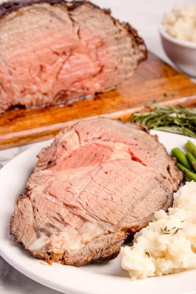 Slice of boneless prime rib on a white dinner plate with mashed potatoes and asparagus.