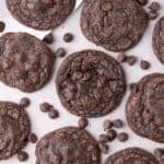 Completed fudge cookies on a parchment lined baking sheet. Chocolate chips are scattered across the baking tray.