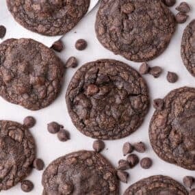 Completed fudge cookies on a parchment lined baking sheet. Chocolate chips are scattered across the baking tray.