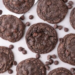 Completed fudge cookies on a parchment lined baking sheet. Chocolate chips are scattered across the baking tray.