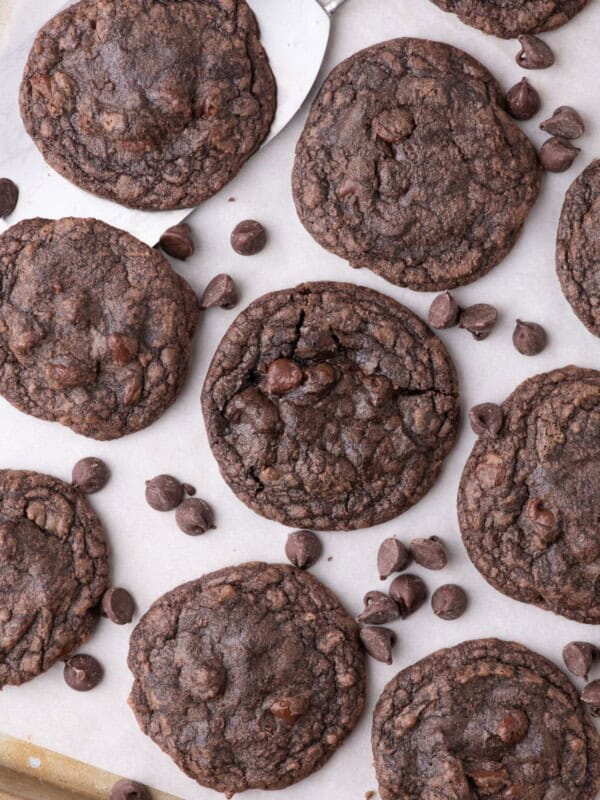 Completed fudge cookies on a parchment lined baking sheet. Chocolate chips are scattered across the baking tray.