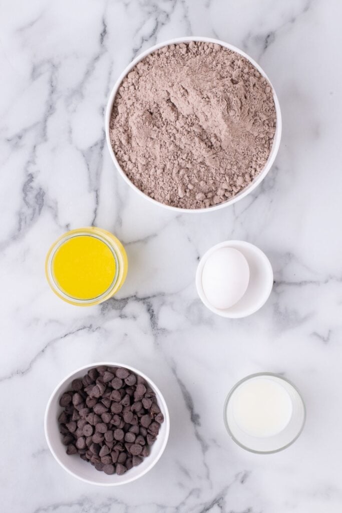 Ingredients for fudge cookies: brownie mix, melted butter, milk, an egg, and chocolate chips.