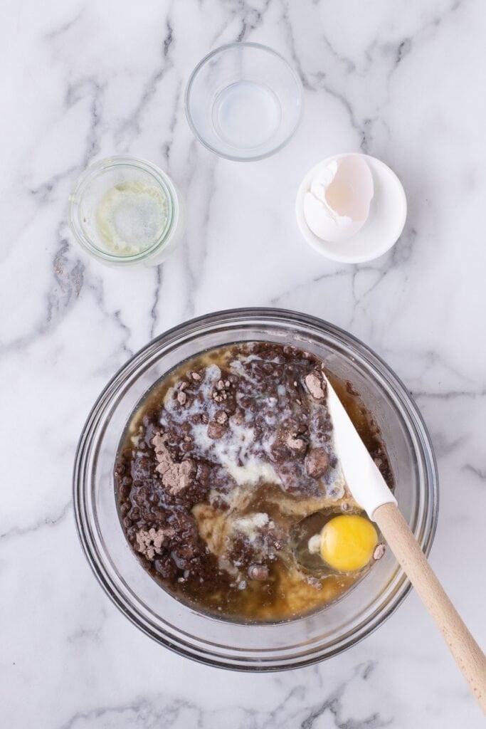 Brownie mix, butter, milk, and an egg being combined together in a glass mixing bowl.