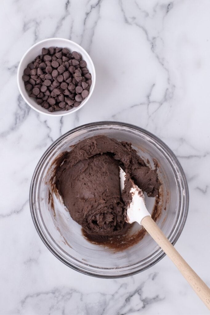 Fudge cookie dough in a glass mixing bowl. A small bowl of chocolate chips is next to it.