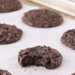A baking sheet with baked cookies one it. One cookie in the center has a bite taken out of it.