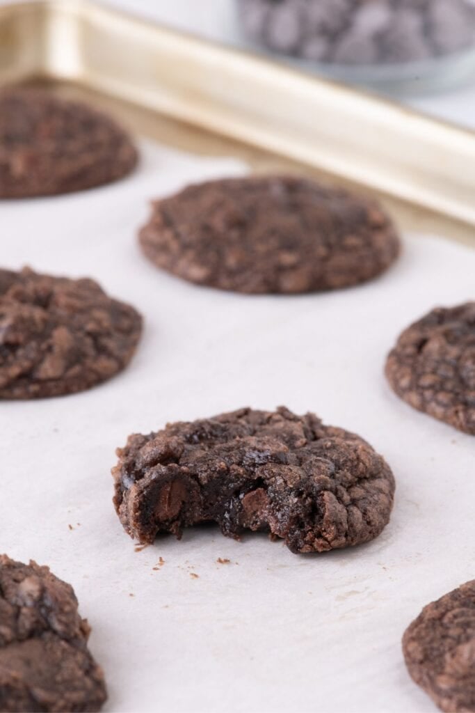A baking sheet with baked cookies one it. One cookie in the center has a bite taken out of it.