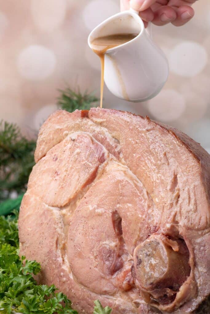 Ham shank drippings being poured over the top of the ham.