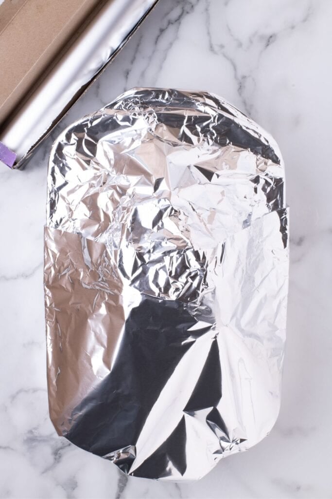 Ham shank covered in foil in a large baking dish.