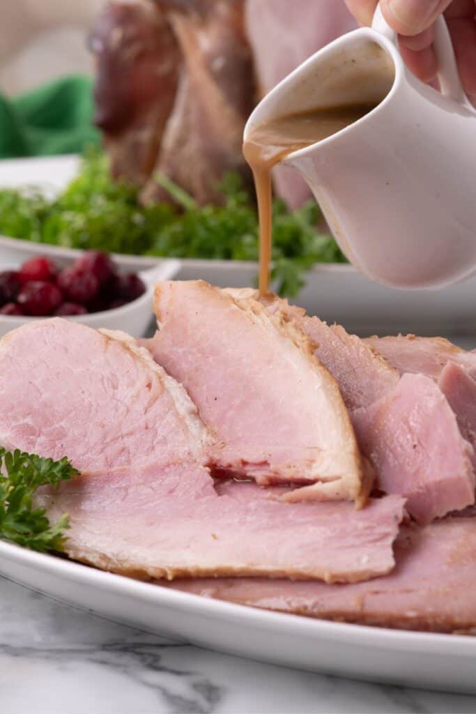 Gravy being poured over slices of ham.