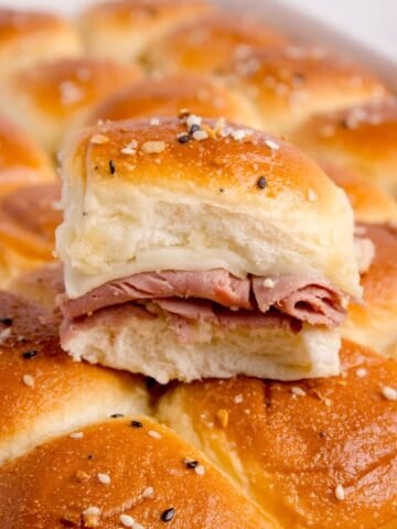 Completed roast beef sliders. One has been cut out of the pan and placed on top of the rest of the sliders in the baking pan.