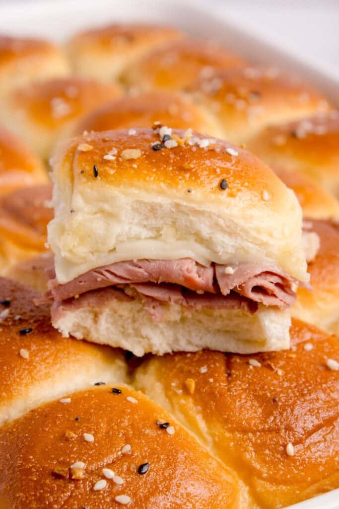 Completed roast beef sliders. One has been cut out of the pan and placed on top of the rest of the sliders in the baking pan.