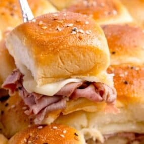 A serving spatula lifting a roast beef slider out of the baking pan.