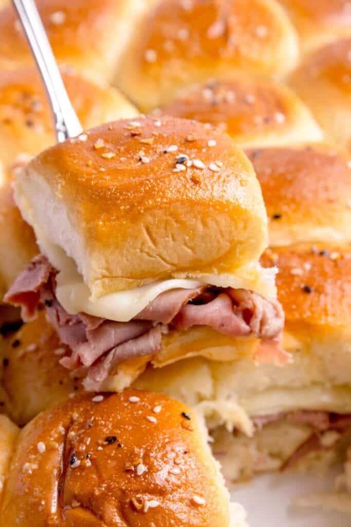 A serving spatula lifting a roast beef slider out of the baking pan.