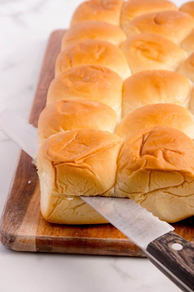 A serrated knife is slicing the brick of rolls in half.