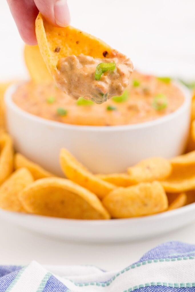 Cheese dip on a corn chip being held over the bowl of dip.