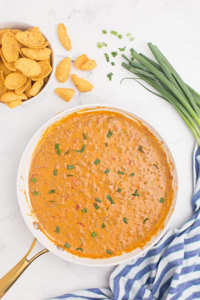 A large skillet with completed cheese dip. A white bowl of corn chips is placed next to the skillet.