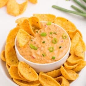 Rotel cheese dip in a white bowl surrounded by a plate of corn chips.