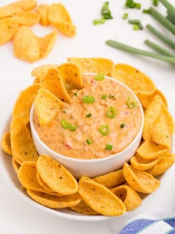 Rotel cheese dip in a white bowl surrounded by a plate of corn chips.