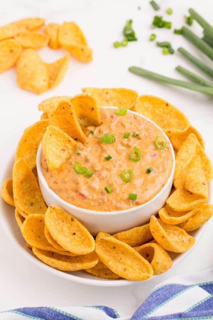 Rotel cheese dip in a white bowl surrounded by a plate of corn chips.