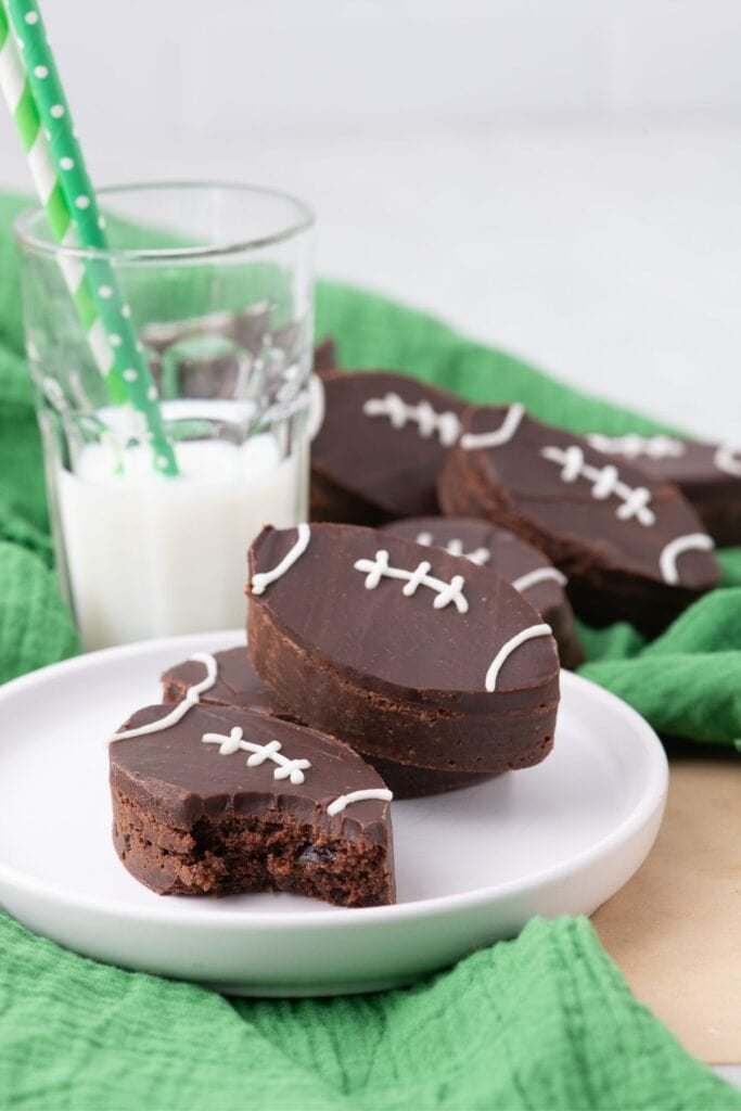 Football brownies stacked on a white plate with a glass of milk next to it.