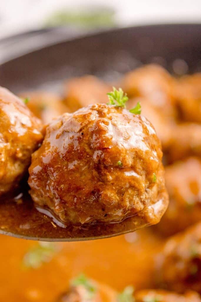 Meatballs on a serving spoon above a cast iron pan with the rest of the recipe.