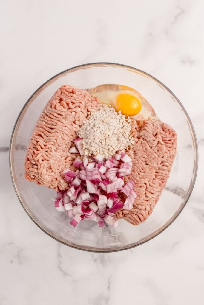 A mixing bowl with ground beef, egg, red onion, and onion soup.