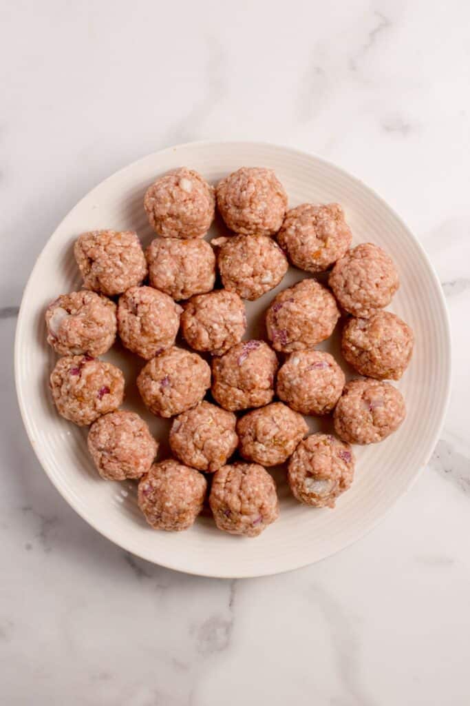 Raw meatballs on a white plate.