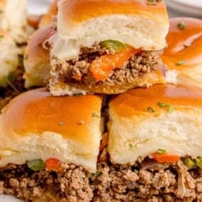 Philly cheesesteak sliders stacked on a parchment covered wooden cutting board.